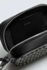 Bandolera pequeña de color negro con cuerpo rectangular y textura trenzada en el frente. Posee un asa de hombro ajustable y extraíble.