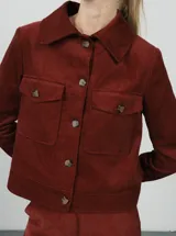 Chaqueta corta negra de pana de algodón con cuello clásico, cierre frontal con botones, dos bolsillos de parche en el pecho y mangas largas.