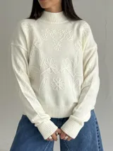 Sweater de punto color blanco con cuello polera, manga larga y diseño bordado al tono con motivos florales en el frente y las mangas.