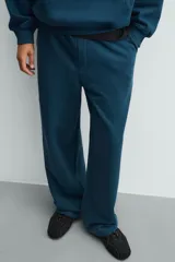 Pantalón jogger de corte relajado y pernera ancha, confeccionado en tejido de algodón con interior perchado. Presenta cintura elástica con cordón interior, bolsillos laterales y un bolsillo trasero de plastrón.
