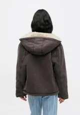Campera con capucha Carhartt WIP modelo Mitch, color marrón oscuro, confeccionada en lona de algodón de peso medio con forro interno de corderito sintético. Cuenta con cierre frontal bidireccional, bolsillos frontales tipo parche y etiqueta cuadrada tejida con el logo de la marca.
