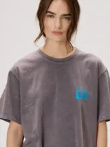 Remera oversize de corte cuadrado, color lila con efecto acid wash, cuello redondo y pequeño gráfico frontal en color rojo.