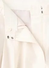 Pantalón sastrero de algodón color marfil, de tiro bajo y diseño recto de pernera ancha. Cuenta con pinzas frontales, bolsillos laterales y un pequeño bolsillo con solapa y botón en la cintura.