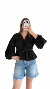 Blusa blanca de manga larga amplia, con escote en V y frunces en el cuerpo. Posee cordones ajustables con lazos en el frente y en la cintura.
