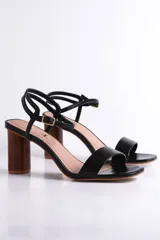 Sandalia de cuero color peltre, con tira ancha sobre los dedos y tira fina con hebilla al tobillo. El taco es cilíndrico de madera clara.