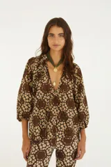 Blusa de corte relajado color marrón con estampado floral de margaritas, escote en V con cordones colgantes y mangas tres cuartos abullonadas con puños elastizados.
