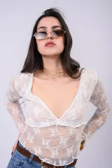 Remera de encaje blanco con transparencia, escote en V pronunciado, detalle fruncido en el busto y mangas largas.