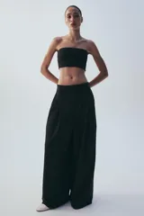 Pantalón de tiro medio color marrón, con pinzas en el delantero, perneras anchas de corte recto y trabillas para cinturón. Cuenta con bolsillos laterales y traseros, y cierre frontal con cremallera y botón.