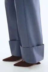 Pantalón sastrero de sarga color azul, de corte recto y pierna ancha, con pliegues frontales y doblez ancho en los bajos.