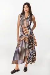 Blusa cruzada sin mangas confeccionada en algodón liviano, con cierre de lazo lateral en la cintura y cuello camisero. Presenta un diseño de rayas verticales y diagonales en tonos marrones, blancos y celestes.