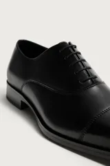 Zapato de vestir tipo oxford color negro, con horma redonda, cordones y suela con ligero tacón.