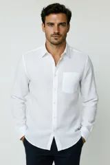Camisa blanca de manga larga, con cuello camisero, cierre frontal de botones y un bolsillo aplicado en el pecho.