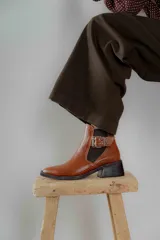 Botineta de cuero charol negro con acabado brillante, diseño de punta fina y taco cuadrado. Presenta un panel elástico lateral y una correa decorativa con hebilla metálica plateada.
