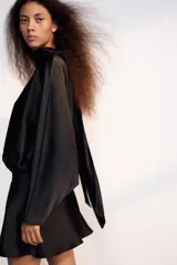 Vestido corto negro de tejido satinado, con cuello alto, mangas largas amplias y detalle de frunces en la cintura.