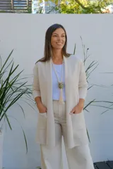 Saco abierto tipo cárdigan color crudo, de corte recto y largo medio, con mangas largas y dos bolsillos frontales aplicados.