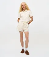 Short femenino de tiro alto color crudo, confeccionado en sarga con textura floral calada de broderie. Cuenta con cintura elástica y cordón ajustable para anudar.