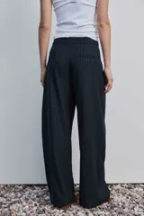 Pantalón de vestir de corte ancho y relajado, color negro con sutiles rayas diplomáticas verticales. Presenta bolsillos laterales y cierre frontal oculto.