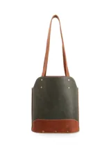 Matera de diseño vertical con cuerpo en cuero verde oscuro y base en cuero color suela. Presenta correas largas fijas, detalles de remaches metálicos dorados y logo de la marca grabado en la parte superior.