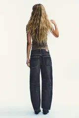 Jeans de tiro medio con diseño baggy barrel, cinco bolsillos y costuras laterales torcidas. Presenta cierre frontal con cremallera y botón metálico.