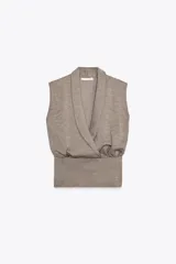 Top sin mangas confeccionado en tejido piqué, con escote cruzado tipo solapa y detalle de pliegues. Presenta una banda ancha ajustada en la cintura y un diseño de hombros caídos.