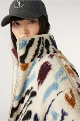 Campera bomber reversible con un lado de corderito estampado con manchas abstractas en tonos negro, marrón, azul y violeta sobre fondo blanco, y del otro lado liso en tono crudo.