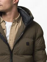 Campera puffer color verde militar, con diseño capitoneado, cuello alto y capucha integrada. Cuenta con cierre frontal, bolsillos laterales con cierre y puños con ojal para el pulgar.