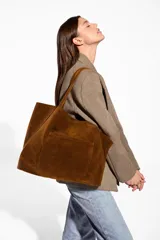 Cartera tipo tote bag de gamuza color marrón, amplia, con doble asa larga para llevar al hombro y bolsillo exterior frontal.
