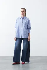 Camisa a rayas verticales blancas y marrones, de manga larga con puños abotonados, cuello camisero y botones frontales. Incluye un bolsillo en el pecho con bordado sutil.