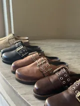 Zueco de cuero color beige, con hebilla metálica y remaches.