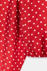 Chaqueta roja con estampado de lunares blancos, cuello subido, manga larga con puños plisados, bolsillos delanteros, bajo ajustable con cordón y cierre frontal con cremallera.
