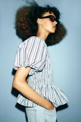 Top de cuello redondo con cuerpo de nido de abeja elástico y mangas cortas abullonadas con elástico en los puños. Presenta un diseño de rayas verticales en tonos azul, rojo y negro, con un bajo estilo peplum y cierre de botón en la espalda.