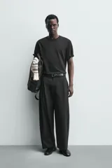 Pantalón chino de corte wide fit confeccionado en tejido de algodón. Presenta pliegues frontales, bolsillos laterales y bolsillos traseros de vivo, con cierre frontal de cremallera y botón.