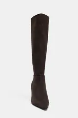 Bota de caña alta confeccionada en serraje, con diseño de punta fina y tacón fino. Presenta detalle de pespuntes en el cuerpo y sistema de calce pull-on.