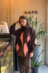 Camisa marrón de poplin con corte regular, cuello clásico, mangas largas con puños abotonados y cierre frontal con botones. Presenta apliques de rombos rosados en el frente y los codos.