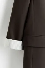 Blazer de sarga con solapas de pico, diseño de frente abierto y bolsillos delanteros con solapa. Presenta mangas con forro a rayas diseñado para ser remangado.