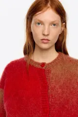 Cardigan corto de corte globo confeccionado en mezcla de alpaca, con botones frontales, escote caja y manga larga con forma. Presenta un diseño bicolor con bloques de color rojo y marrón.