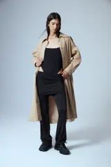 Trench midi de color camel, confeccionado en una mezcla de algodón y nylon con propiedades repelentes al agua. Presenta un diseño clásico con cuello camisero, cierre frontal de botones, bolsillos laterales y tajos en los costados.