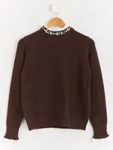 Sweater de punto color beige, con cuello redondo adornado con apliques de pedrería y detalle de puntilla blanca en el cuello y los puños.