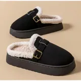 Pantuflas de plataforma con exterior de gamuza y forro interior de corderito sintético. Presentan un diseño sin talón con una tira decorativa ajustable mediante hebilla metálica lateral.