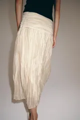 Falda midi confeccionada en hilatura con mezcla de lyocell, de tiro medio y cintura drapeada con forro interior combinado a tono. Presenta un diseño plisado con bajo recto y cierre lateral con cremallera oculta en costura.