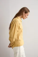 Camisa amarilla de manga larga con detalles bordados y calados en los hombros, pecho y mangas, corte clásico con cuello camisero y cierre frontal de botones.