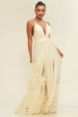 Vestido largo de fiesta en color crema con escote en V profundo y tirantes finos. Presenta una falda fluida con una abertura lateral y un delicado diseño floral bordado en relieve sobre toda la prenda.