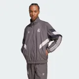 Chaqueta deportiva Adidas del Real Madrid en color gris, con diseño de bloques en blanco y azul marino, cuello alto, cierre frontal y las icónicas tres tiras en las mangas.