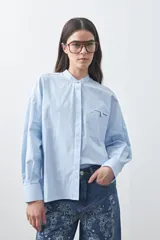 Camisa de manga larga en color celeste, con cuello mao y cierre frontal oculto. Presenta un diseño de silueta relajada con sisa caída y un bolsillo aplicado en el pecho.