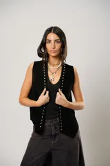 Chaleco de cuero gamuzado negro con diseño oversize, decorado con tachas metálicas a lo largo de los bordes frontales. Presenta una terminación en picos en el ruedo y flecos en la parte posterior.