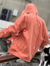 Campera con capucha de color salmón, con cierre frontal y botones a presión en el ruedo. Diseño holgado de manga larga con puños elásticos.