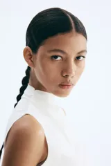 Top sin mangas color blanco hueso, de tejido liso y corte ajustado, con cuello alto tipo mock neck y bordes sin rematar.