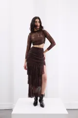 Falda midi de encaje color marrón, con diseño de tiro alto, fruncido en la parte frontal y abertura lateral pronunciada con terminación en volados asimétricos.