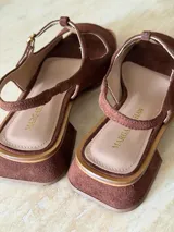 Sandalia de gamuza color marrón, con diseño tipo T-strap, taco cuadrado bajo y tira ajustable al talón con hebilla metálica dorada.