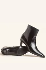 Bota de caña corta confeccionada en cuero vacuno color chocolate con acabado brillante. Presenta punta fina, cierre posterior y taco chupete bajo.